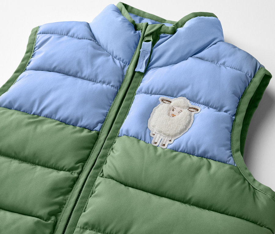 Detailansicht einer Kinder-Steppweste mit Colorblocking und Schaf-Applikation.
