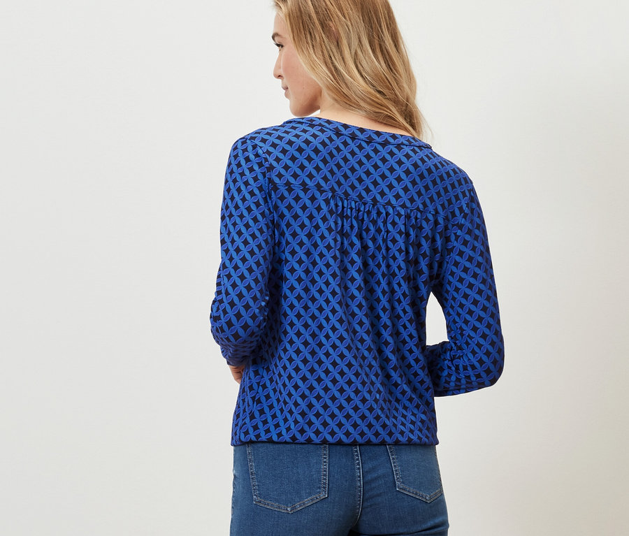 Frau trägt ein bedrucktes Blusenshirt in Kobaltblau und Jeans.