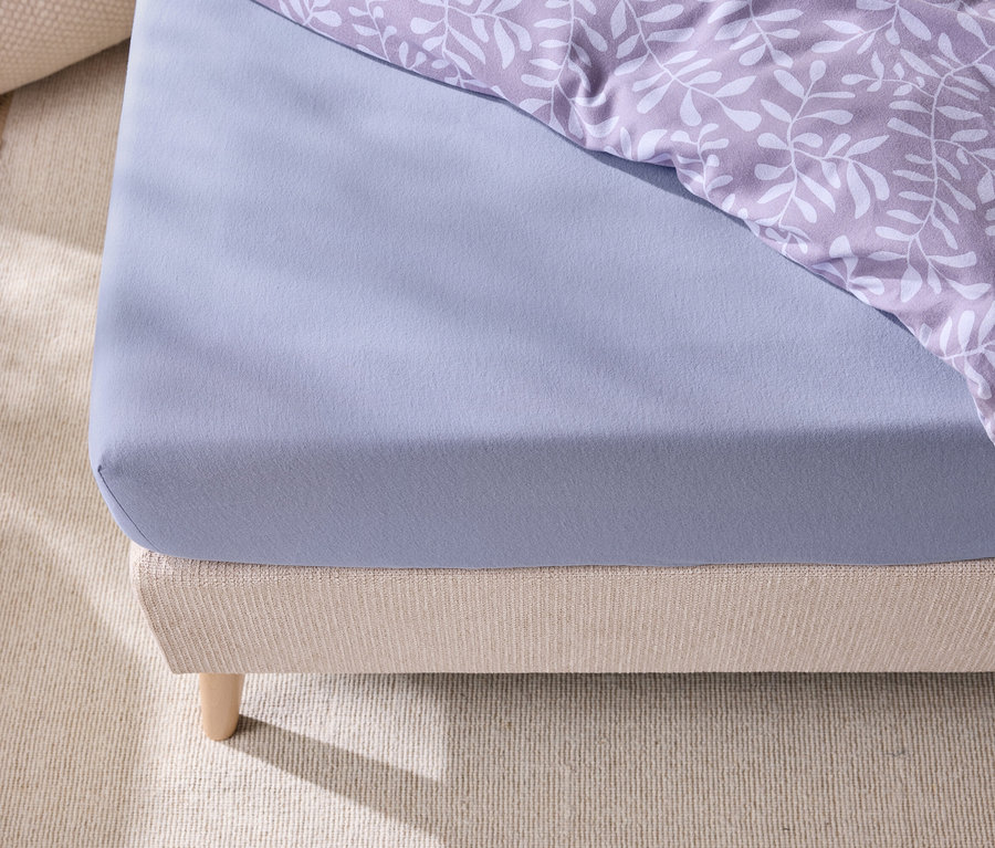 Detailansicht eines Bettes mit einem blauen Spannbettlaken und Bettwäsche mit Blattmuster.