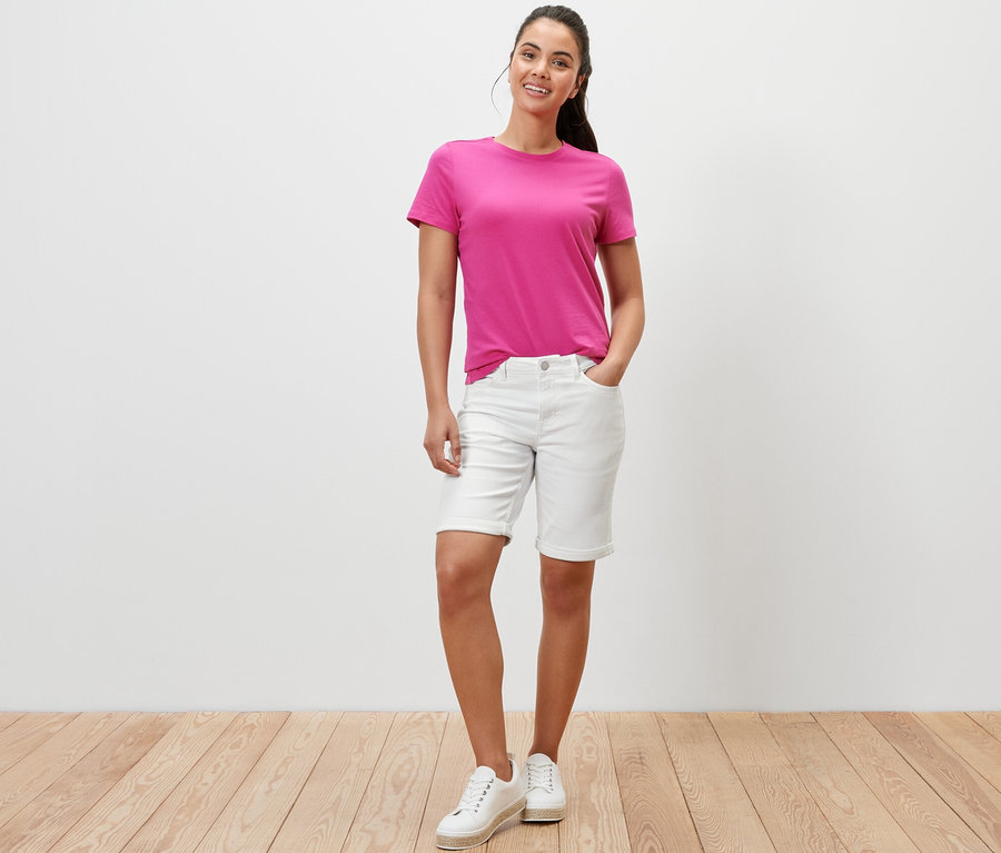 Eine Frau posiert in cremeweißen Denim Shorts ‒ Fit »Lea« und einem pinken T-Shirt.