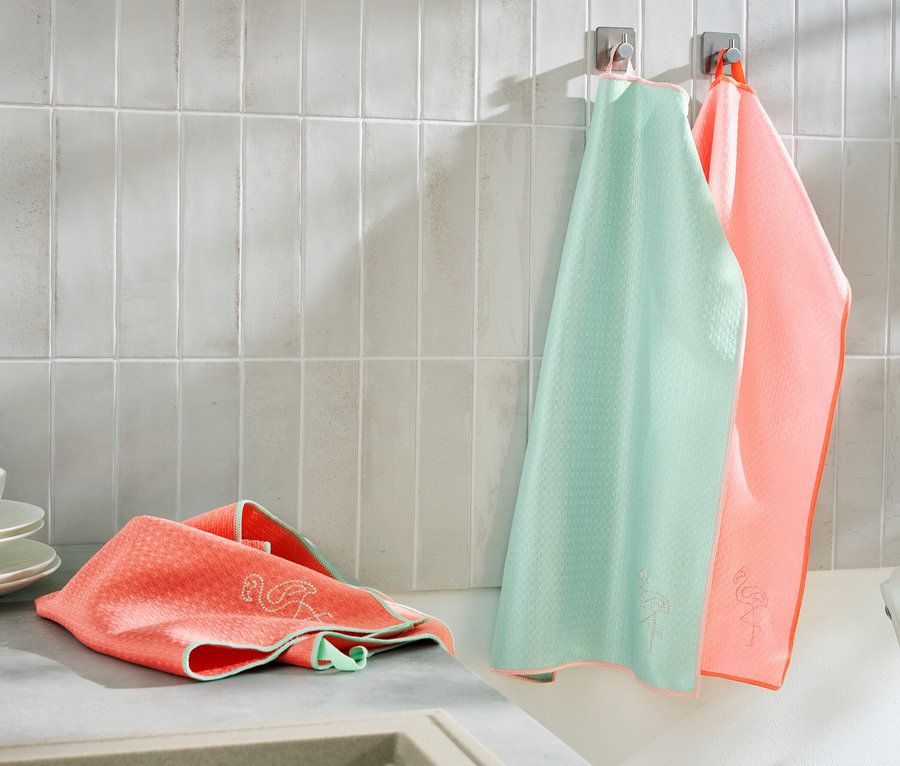 Zwei 3 Geschirrtücher hängen an der Wand und eines liegt neben Tellern auf der Küchentheke.