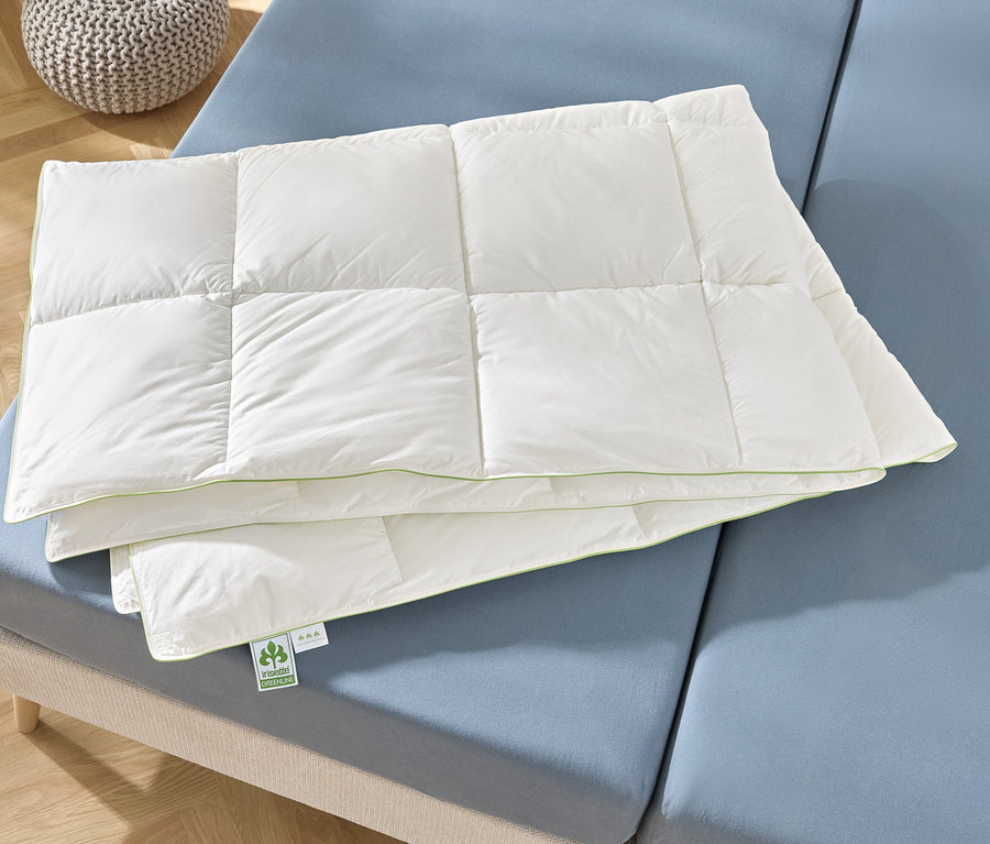 Eine gefaltete, weiße Steppdecke liegt auf einem blauen Bett.