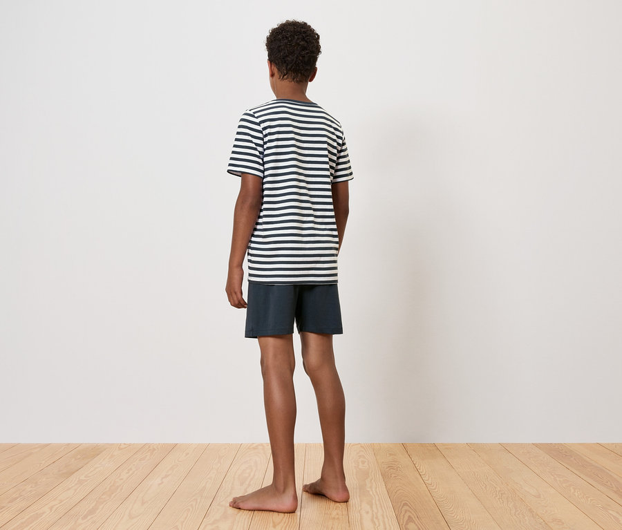 Junge steht mit dem Rücken zum Betrachter, trägt ein gestreiftes T-Shirt und Shorts.