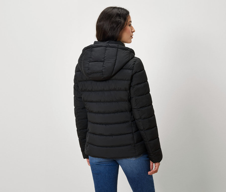 Eine von hinten gezeigte Frau trägt eine schwarze Steppjacke mit Kapuze und Jeans.