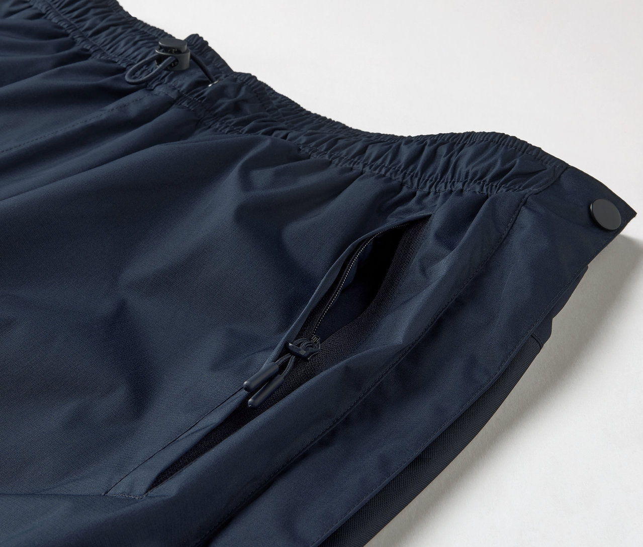Detailaufnahme einer High-Tech-Regenhose mit durchgehendem Reißverschluss, die einen elastischen Bund mit Kordelzug und eine Reißverschlusstasche zeigt.