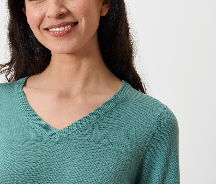 Porträt einer lächelnden Frau in einem türkisfarbenen V-Ausschnitt Pullover.