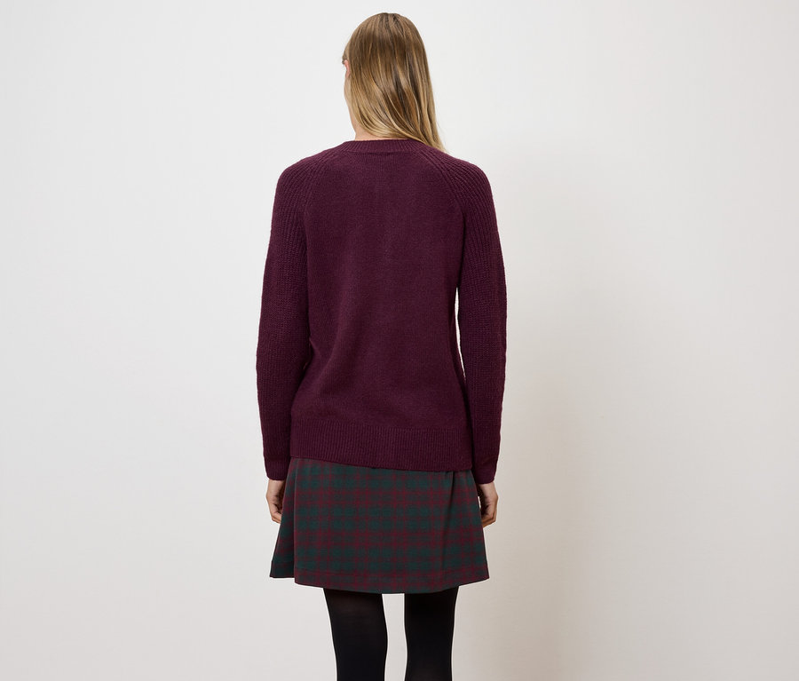 Frau von hinten trägt einen weinroten Pullover und einen karierten Rock.