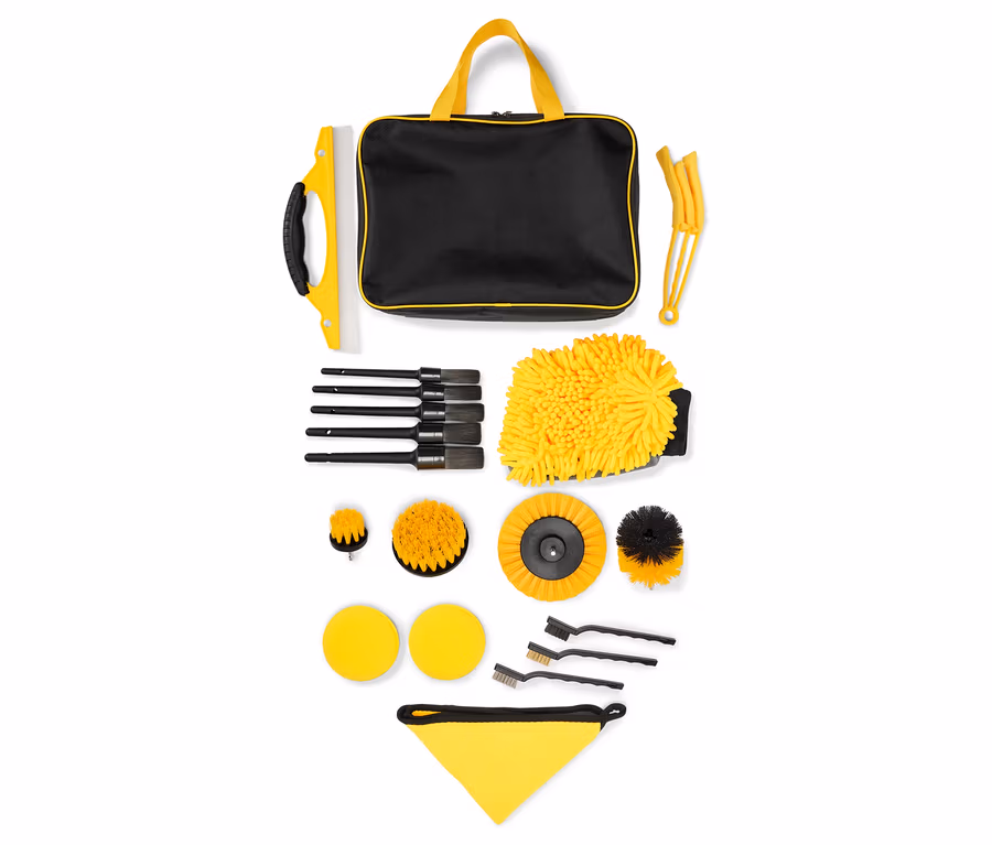 Ein Autoreinigungsset mit einer schwarzen Tasche mit gelben Griffen, einem gelben Waschhandschuh und verschiedenen Bürsten.