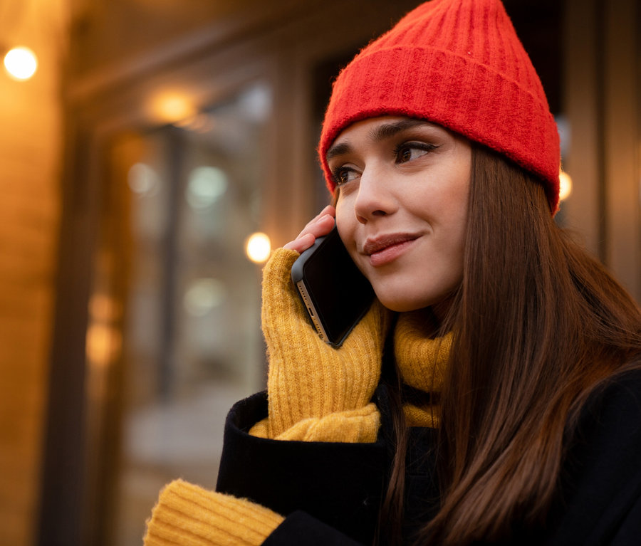 Frau mit roter Mütze und gelben Handschuhen telefoniert.