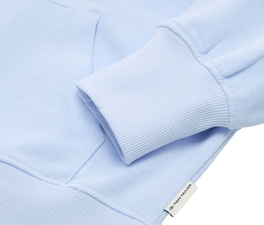 Detailansicht eines hellblauen Kapuzenpullovers mit geripptem Ärmelsaum. Ein Tom Tailor Etikett ist sichtbar.