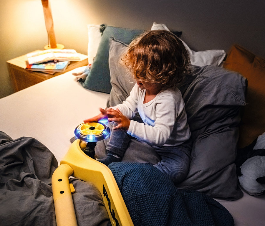 Kind spielt mit gelbem PUKY Roller PUSH auf dem Bett.