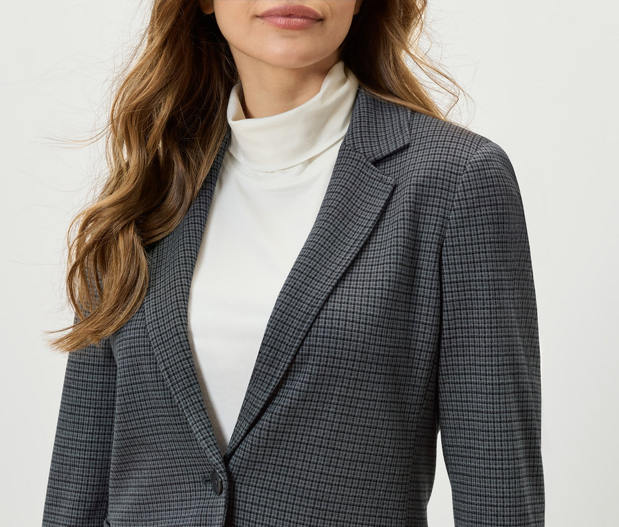 Frau trägt einen karierten Blazer und einen weißen Rollkragenpullover.