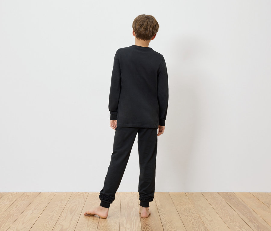 Ein Kind steht barfuß vor einer weißen Wand und trägt einen schwarzen MINECRAFT Kinder-Pyjama.