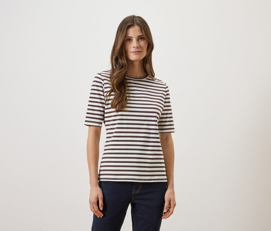 Frau mit langen braunen Haaren, die ein gestreiftes T-Shirt und Jeans vor einem weißen Hintergrund trägt.
