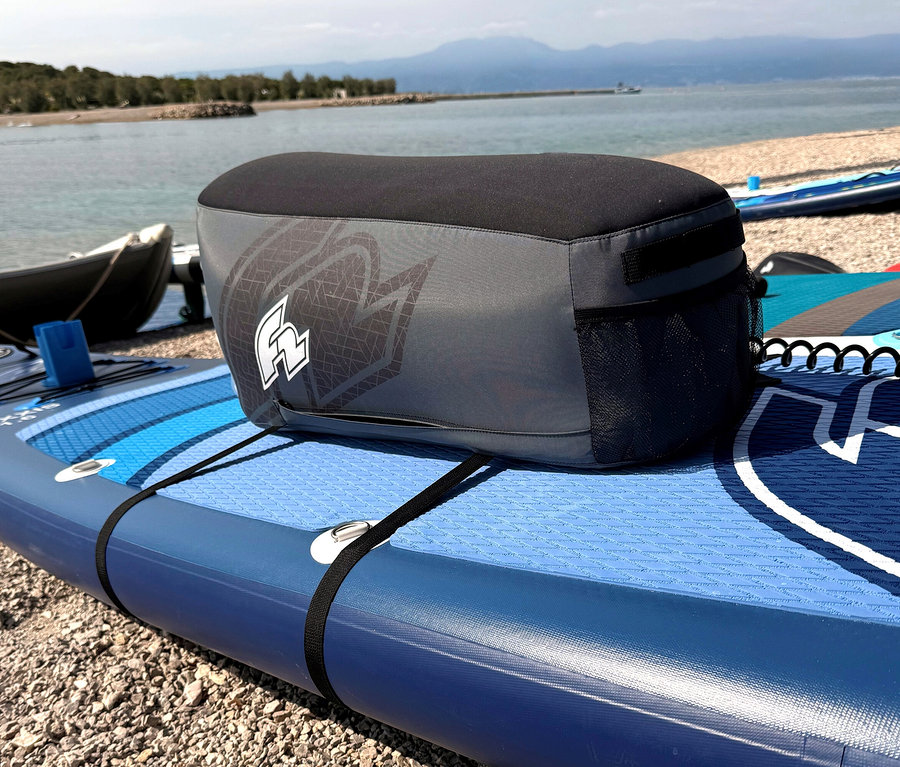 Eine graue Kühltasche mit schwarzem Oberteil steht auf einem blauen Stand-Up-Paddleboard am Strand.