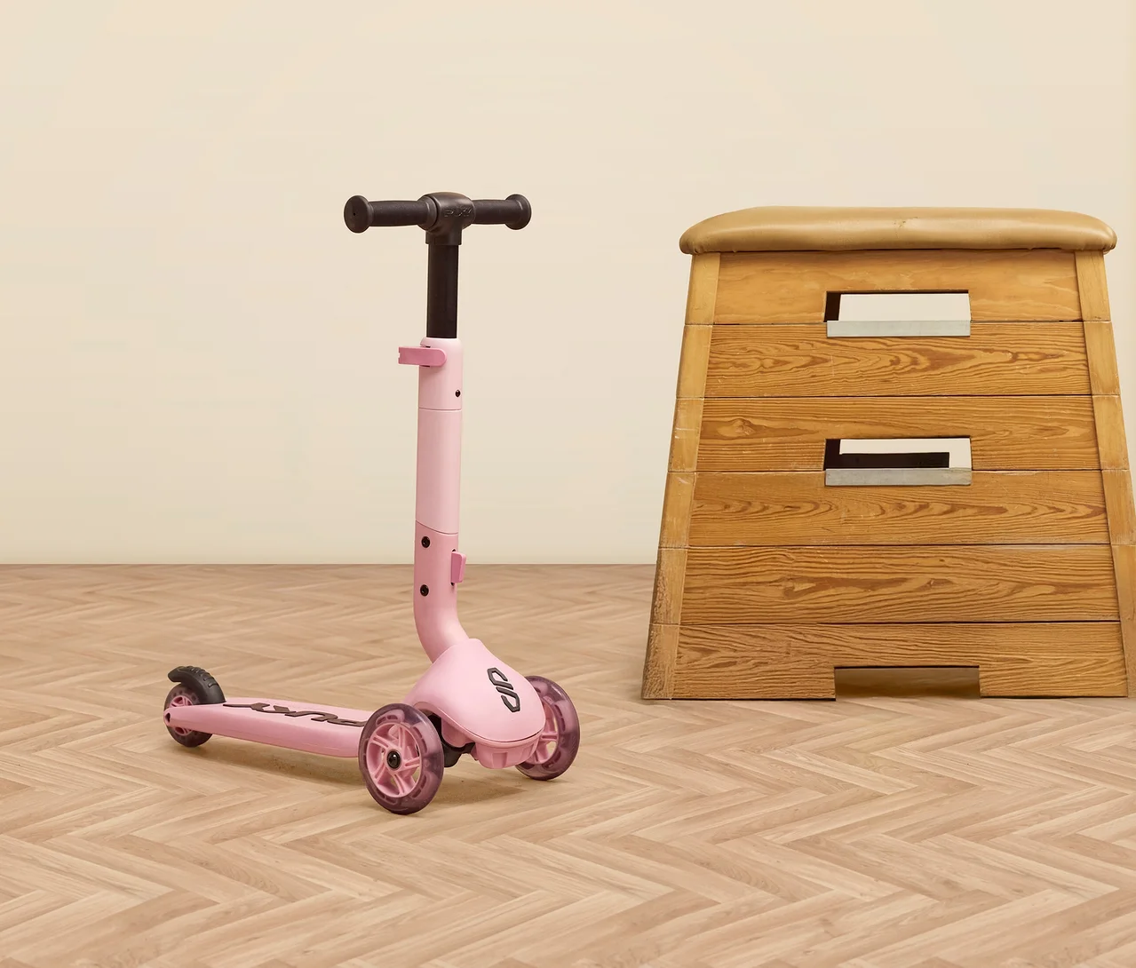 Ein rosa PUKY Roller PUSH steht neben einem Turnbock auf einem Holzboden.