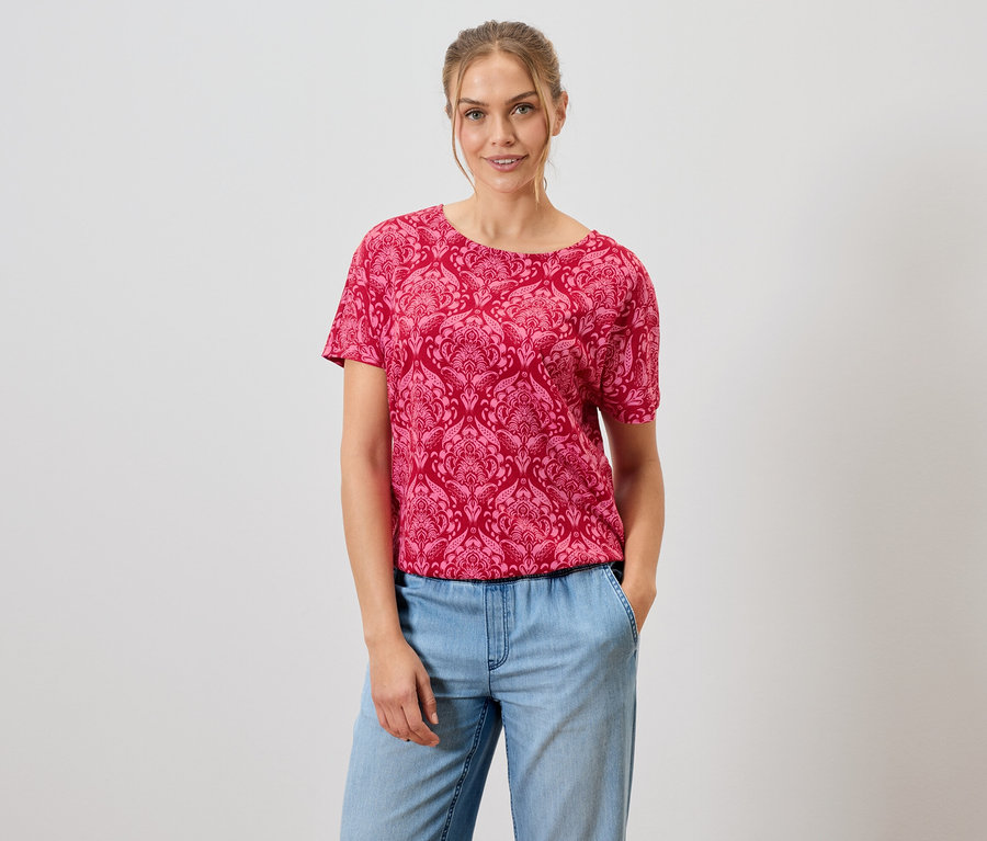Frau trägt ein rotes, gemustertes T-Shirt und blaue Jeans.