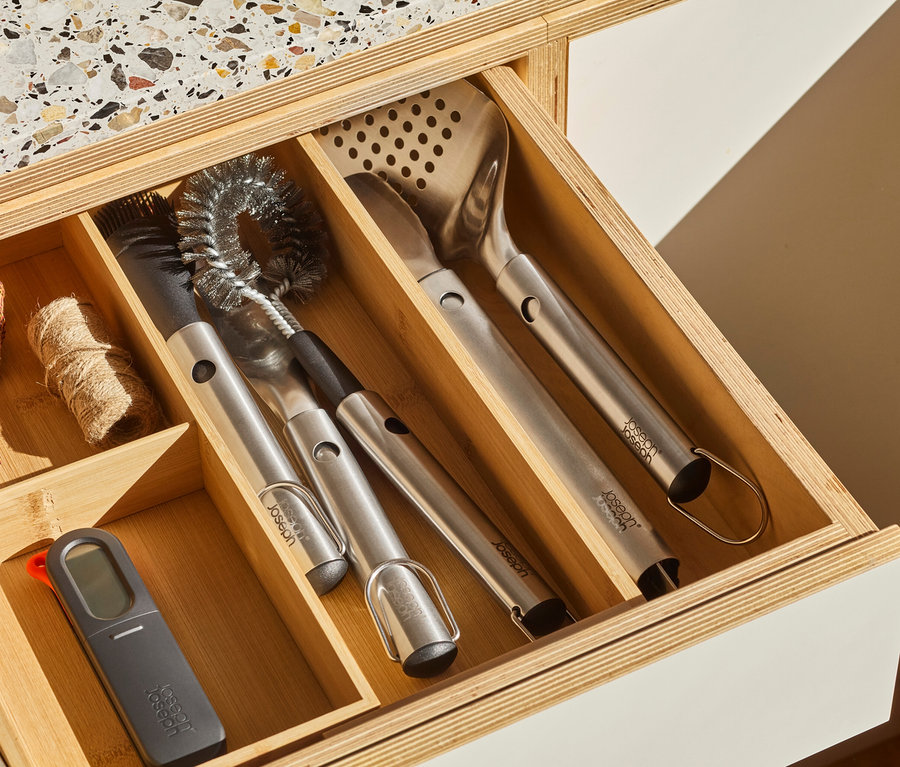 Grillbesteck und ein digitales Thermometer liegen in einer Schublade mit Holzeinsatz.