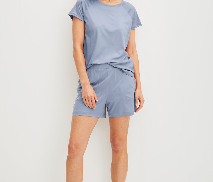 Frau steht barfuß und trägt ein blaues T-Shirt und Shorts.