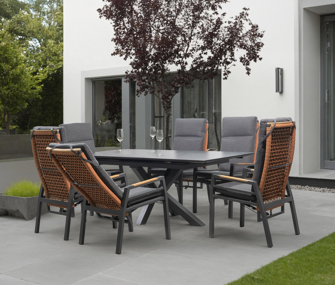 Gartenset mit Esstisch und sechs Stühlen mit grauen Polstern und Rattangeflecht auf einer Terrasse.