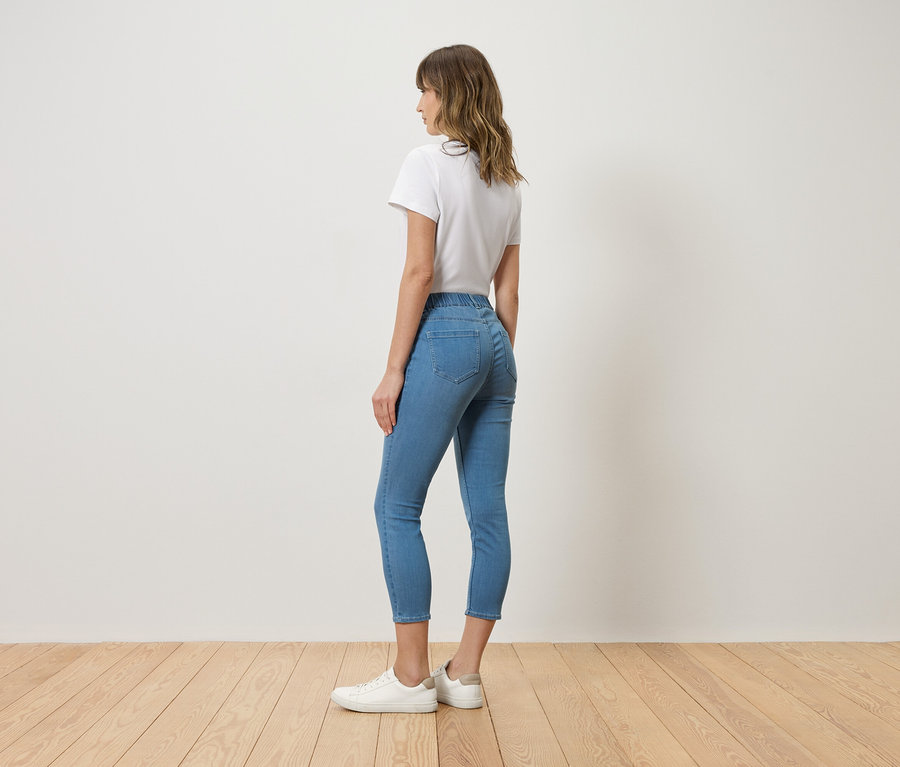 Frau von hinten, mit weißem T-Shirt, blauen Jeans und weißen Turnschuhen.