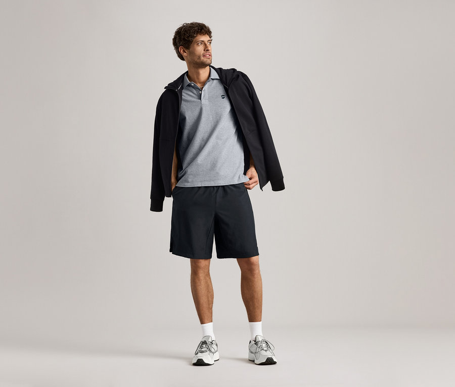 Mann trägt eine Sweatjacke über einem grauen Polohemd, kombiniert mit Shorts.