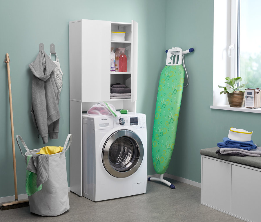 Im Waschraum stehen eine Waschmaschine neben einer weißen Sitzbank mit Schuhfach, ein Bügelbrett und ein Wäschekorb.