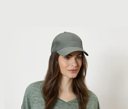Frau mit grüner Baseballkappe und grünem Oberteil vor einem weißen Hintergrund.