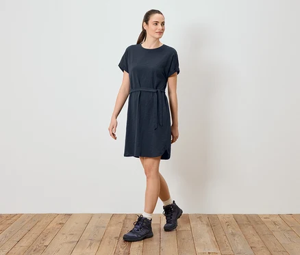 Frau trägt ein blaues T-Shirt-Kleid mit Gürtel und Wanderschuhe.