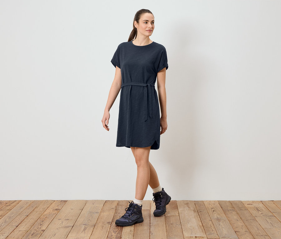 Frau trägt ein blaues T-Shirt-Kleid mit Gürtel und Wanderschuhe.