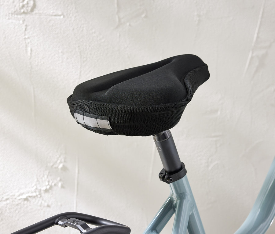 Nahaufnahme eines Fahrradsattels mit schwarzem Bezug und Reflektorstreifen vor einer weißen Wand.
