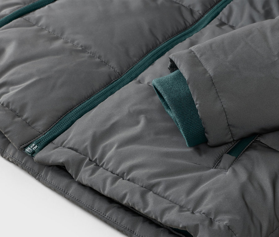 Nahaufnahme einer dunkelgrauen Steppjacke mit grünem Reißverschluss und grünem Rippbündchen.
