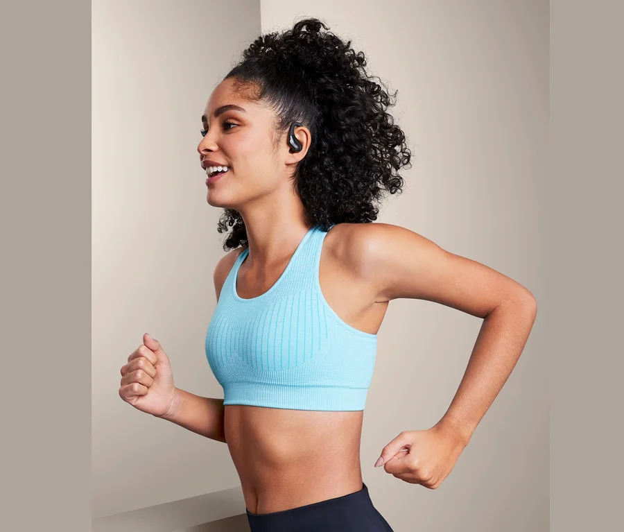 Frau mit blauem Sport-BH und schwarzen Leggings läuft und trägt TWS-In-Ear-Sport-Kopfhörer.