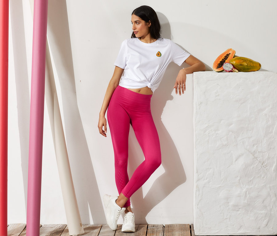 Frau posiert in pinken Sporttights und einem weißen T-Shirt mit Knoten.
