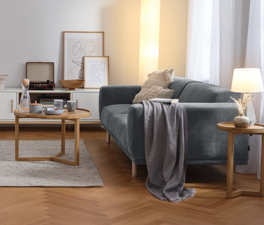 Wohnzimmer mit blau-grauem SCAPA 3-Sitzer-Sofa, Stehleuchte mit Textilschirm und Couchtisch rund.