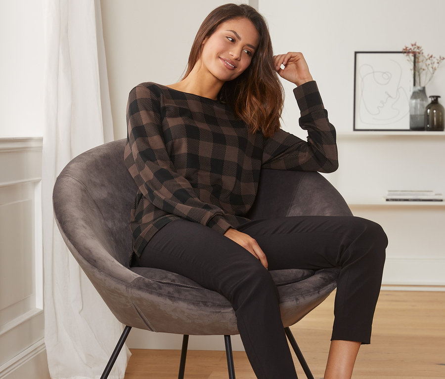 Frau sitzt in einem Sessel und trägt ein kariertes Sweatshirt.