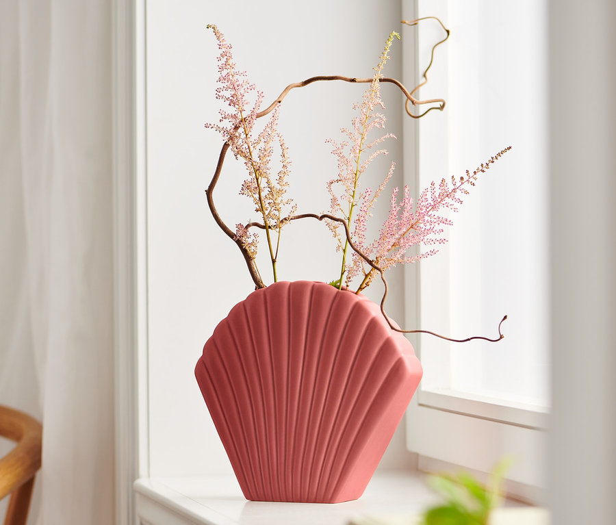 Dekorative Muschel-Vase mit Blumen auf der Fensterbank.