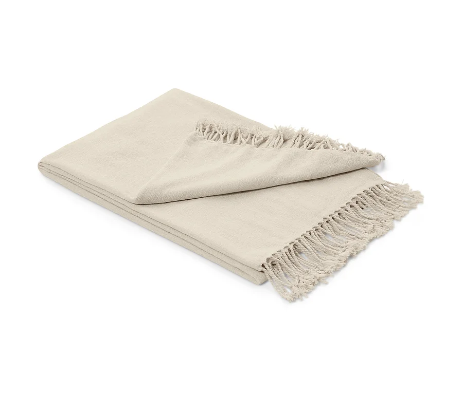 Eine beige Chenille-Wohndecke mit Fransen liegt gefaltet auf einem weißen Hintergrund.