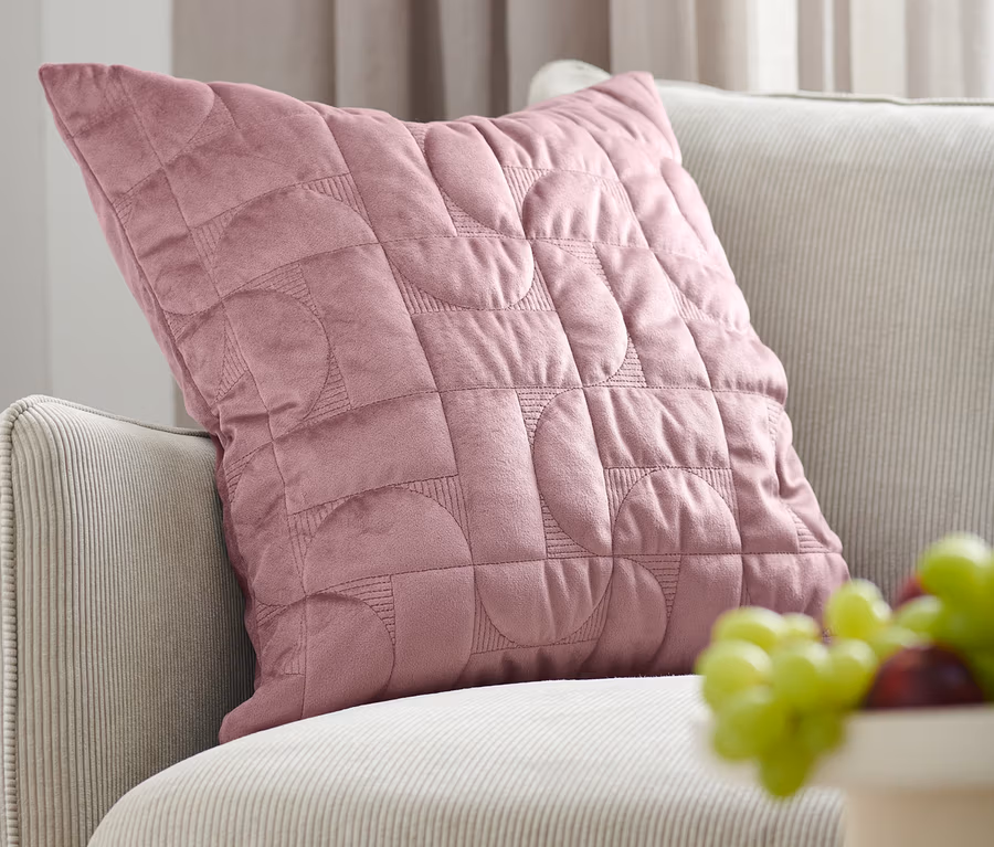 Ein altrosa Samt-Dekokissen-Bezug liegt auf einem beigen Sofa neben einer Schale mit Obst.