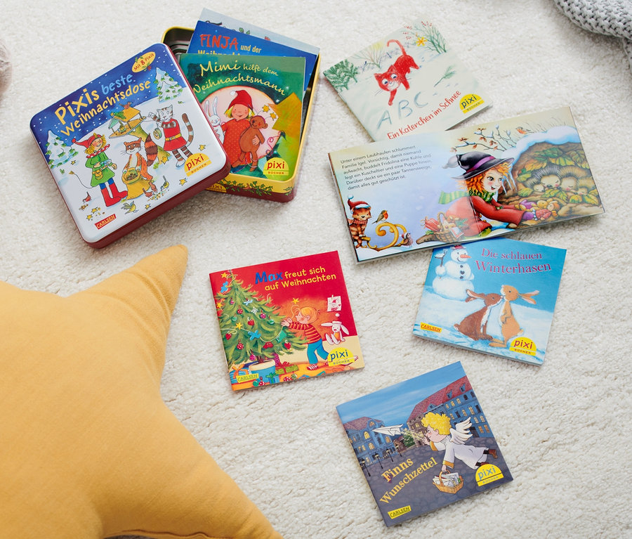 Auf einem weißen Teppich liegen ein Plüschhund, ein gelber Stern und Pixi-Bücher. Eine Bücherbox: »Pixis beste Weihnachtsdose« und mehrere Pixi-Bücher sind verstreut.
