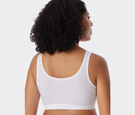 Rückansicht einer Frau mit dunklen lockigen Haaren, die einen weißen SCHIESSER Bustier mit Bio-Baumwolle trägt.