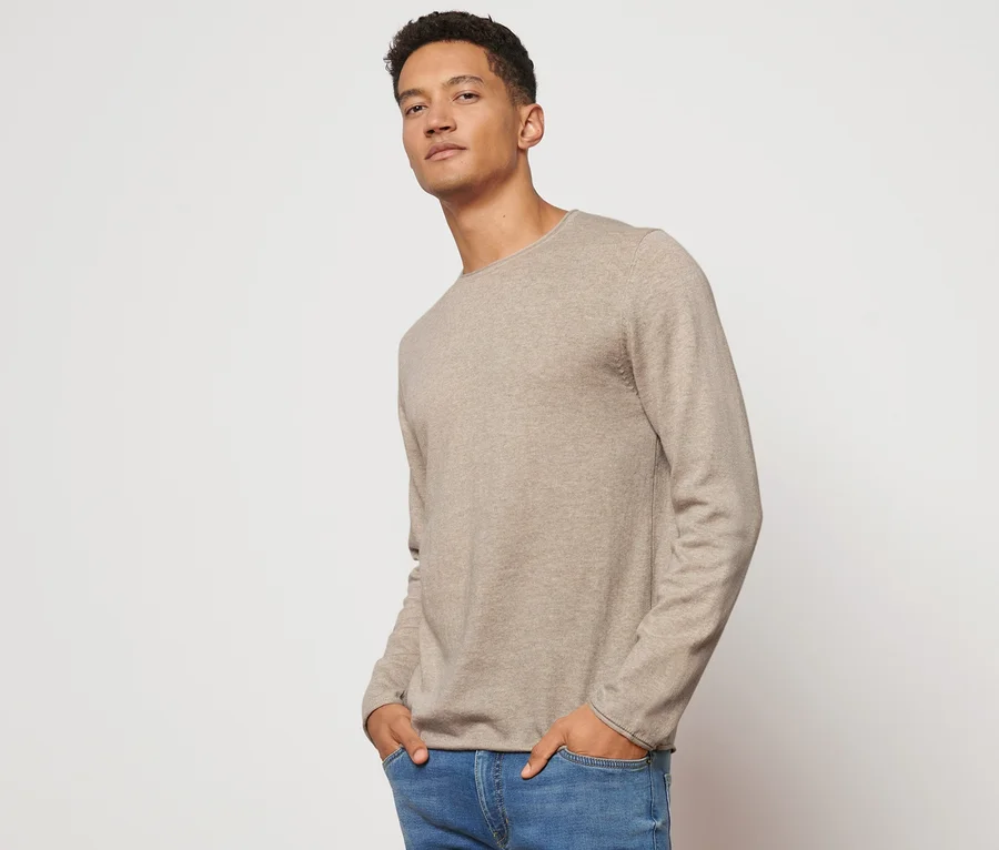 Mann posiert in beigem Pullover.
