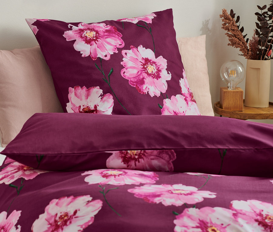 Detailaufnahme von lila Bettwäsche mit Blumenmuster, inklusive Kissen und Teil der Bettdecke.