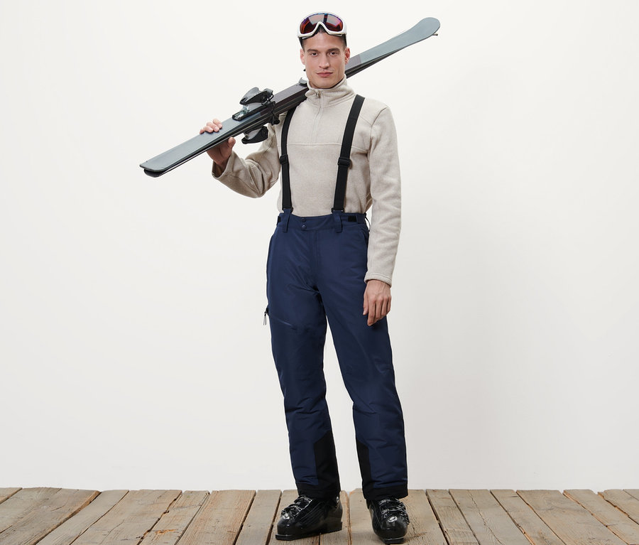 Mann mit Skiern über der Schulter, trägt blaue Skihose.