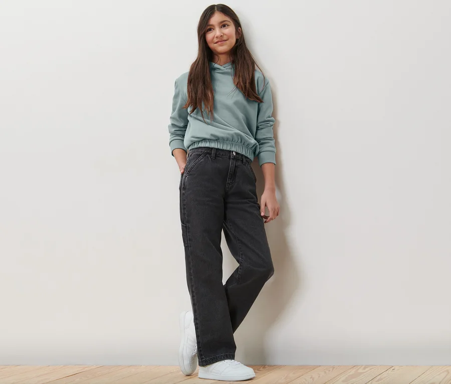 Mädchen posiert in Kinder-Cargohose und Hoodie.