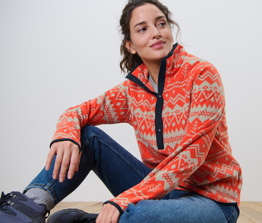 Frau sitzt auf dem Boden und trägt einen Fleecepullover.