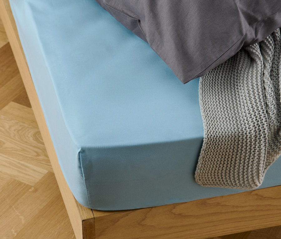 Ein hellblaues Microfaser-Spannbettlaken auf einem Bett mit einem grauen Kissen und einer grauen Strickdecke.