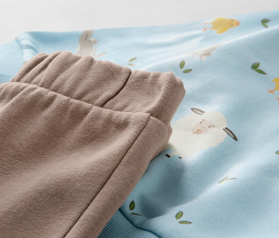 Detail eines Baby-Sweat-Sets mit Lamm- und Kükenmuster.