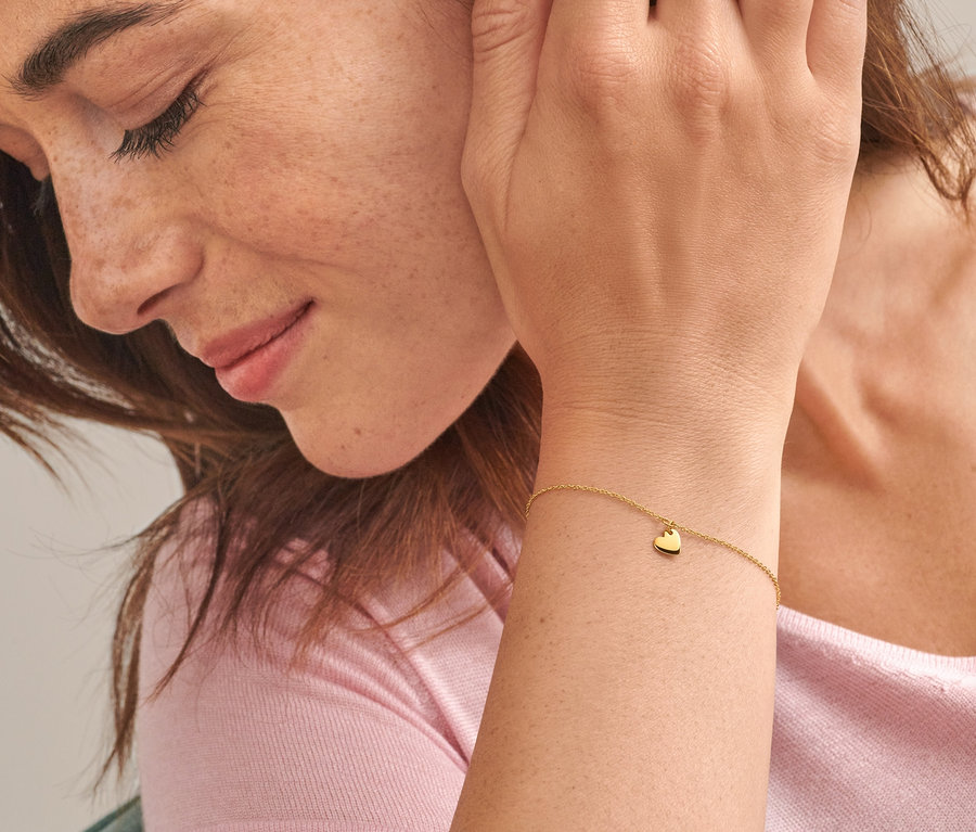 Nahaufnahme einer Frau mit braunen Haaren, die ein Gold-Armband mit Herzanhänger und einen Gold Ring V Zirkonia trägt.