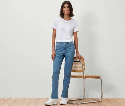 Eine Frau in einem weißen T-Shirt und Straight Jeans ‒ Fit »Kira« steht neben einem Stuhl.